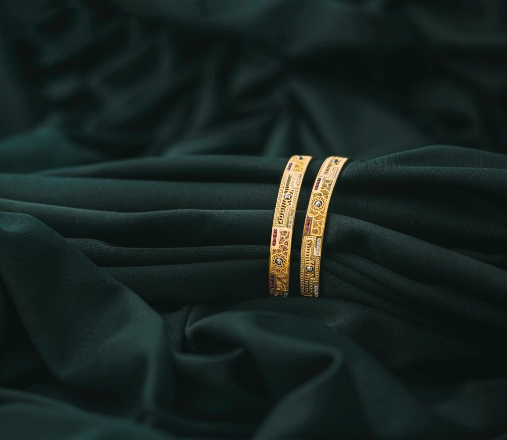 A pair of ornate golden bangles resting on rich, dark green fabric, creating a luxurious and elegant scene.