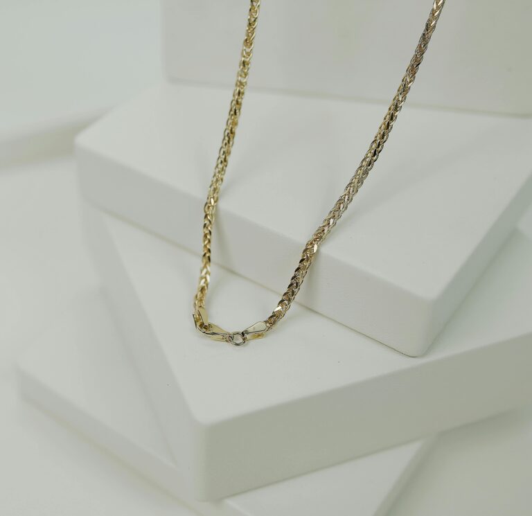 His Highness Close-up of a luxurious gold necklace elegantly displayed on a minimalist white platform.